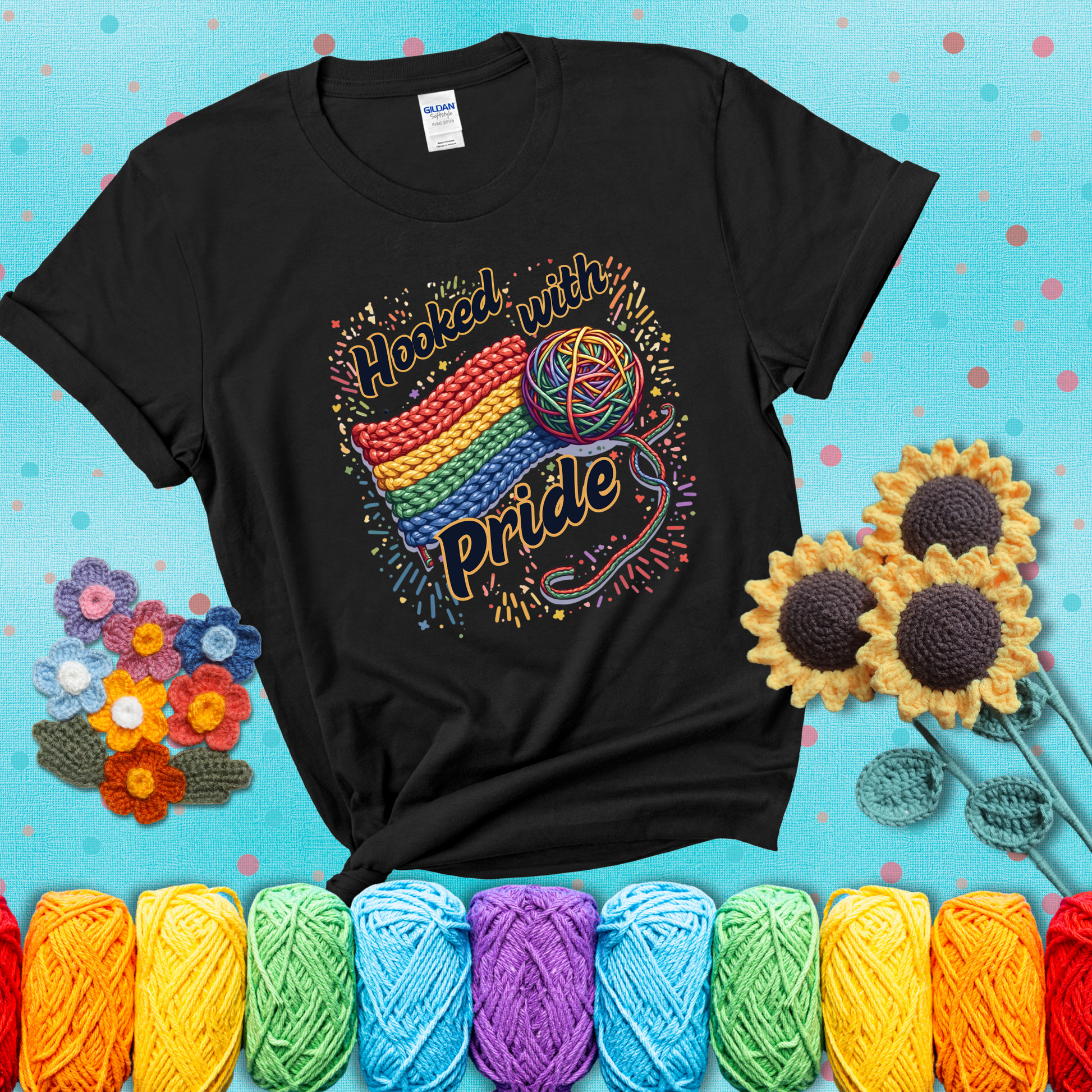 A rainbow-striped crochet swatch paired with a multicolor yarn ball and bold “Hooked With Pride” lettering. Confetti surrounds the vibrant scene showing a black tee with a teal sunflower background