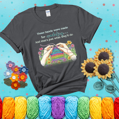 Illustration of two hands crocheting a rainbow swatch, surrounded by vibrant flowers with the phrase “These hands were made for crocheting… and that’s just what they’ll do,” showing a dark grey tee with a teal sunflower background