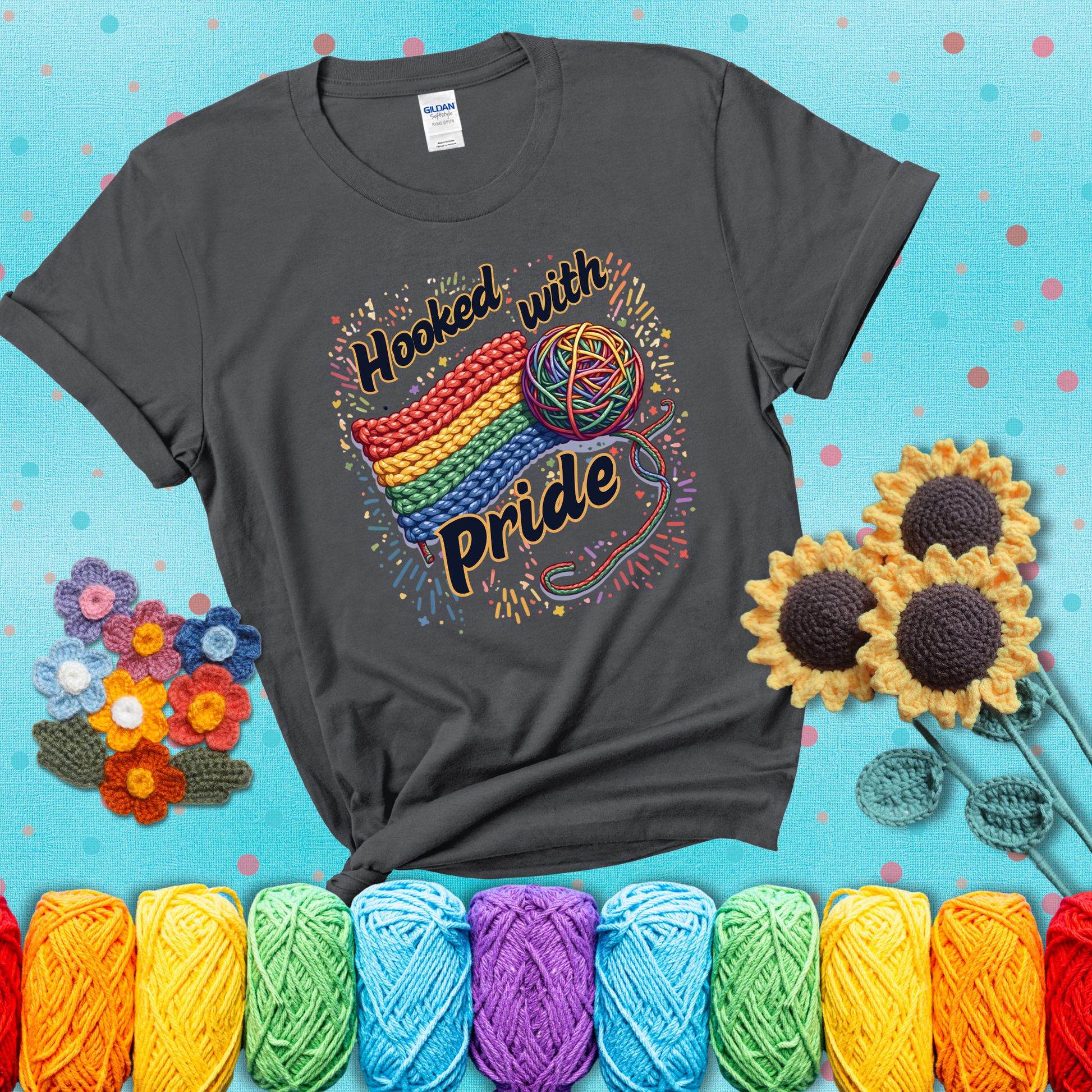 A rainbow-striped crochet swatch paired with a multicolor yarn ball and bold “Hooked With Pride” lettering. Confetti surrounds the vibrant scene showing a dark grey tee with a teal sunflower background
