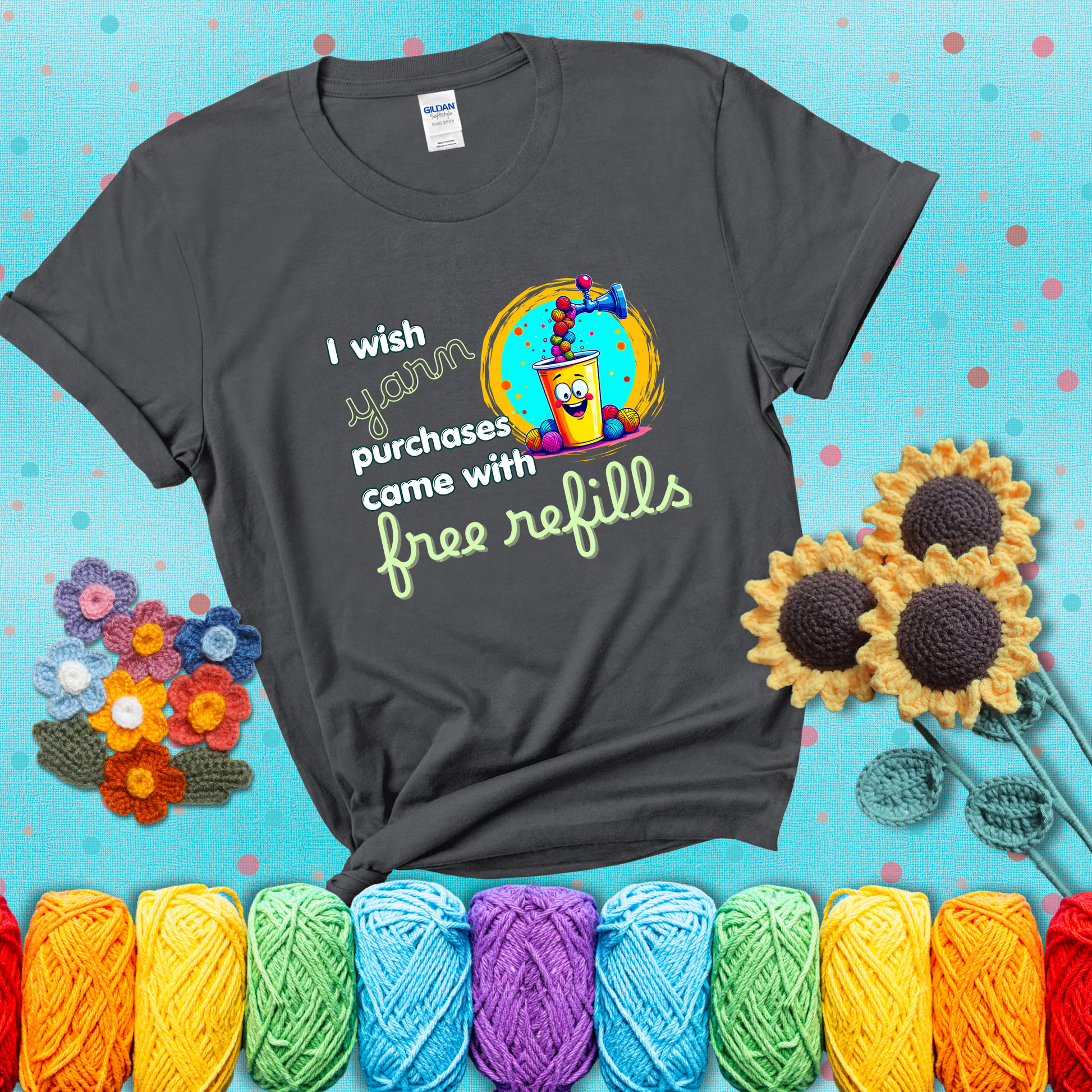 A bright yellow cup with a smiling face is being filled with colorful yarn balls from a soda machine, with the phrase “I wish yarn purchases came with free refills,” showing a dark grey tee with a teal sunflower background