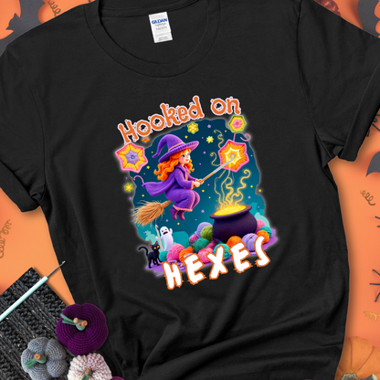 Black t-shirt with stars, hexagon motifs, and a crochet hook, with text reading “Hooked on Hexes.”