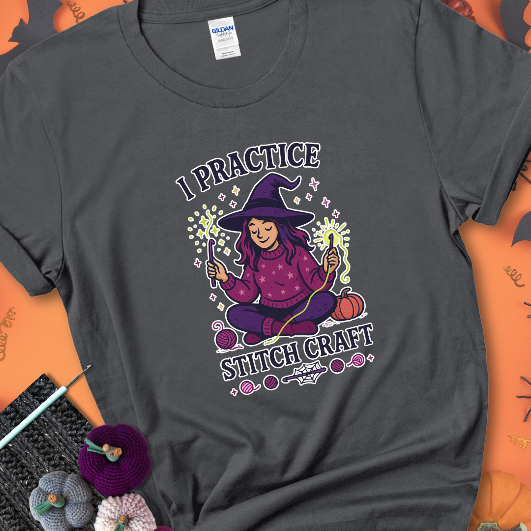 Charcoal t-shirt with a witchy crocheter conjuring glowing yarn with crochet hooks, surrounded by stars and pumpkins, with the phrase “I Practice Stitch Craft.”