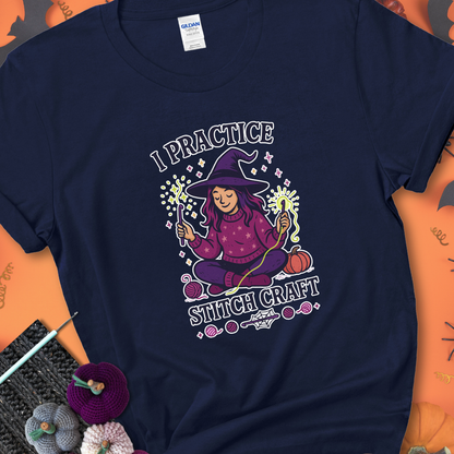 Navy t-shirt with a witchy crocheter conjuring glowing yarn with crochet hooks, surrounded by stars and pumpkins, with the phrase “I Practice Stitch Craft.”