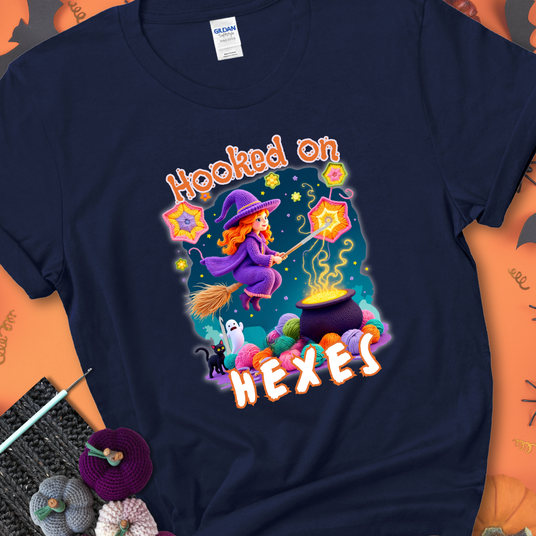 Navy t-shirt with stars, hexagon motifs, and a crochet hook, with text reading “Hooked on Hexes.”