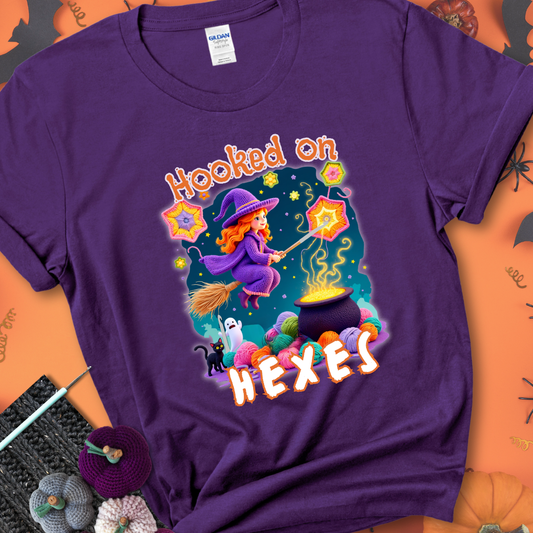 Purple t-shirt with stars, hexagon motifs, and a crochet hook, with text reading “Hooked on Hexes.”