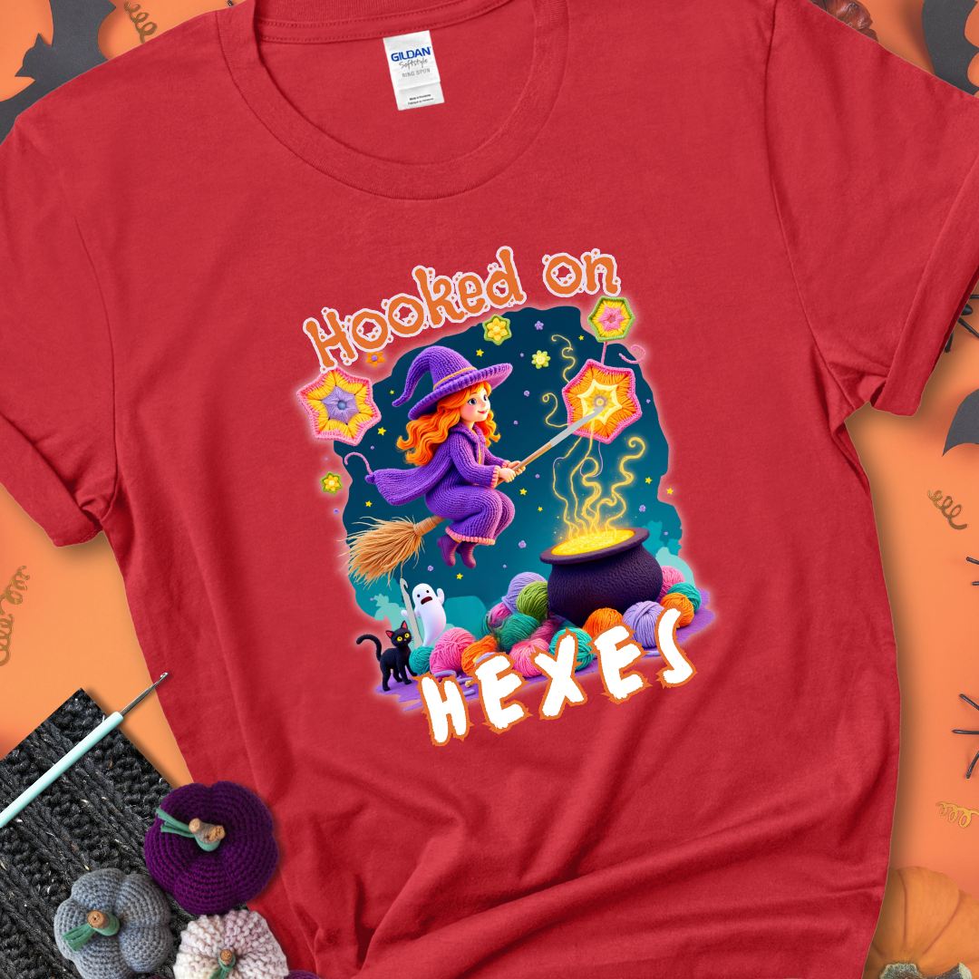 Red t-shirt with stars, hexagon motifs, and a crochet hook, with text reading “Hooked on Hexes.”