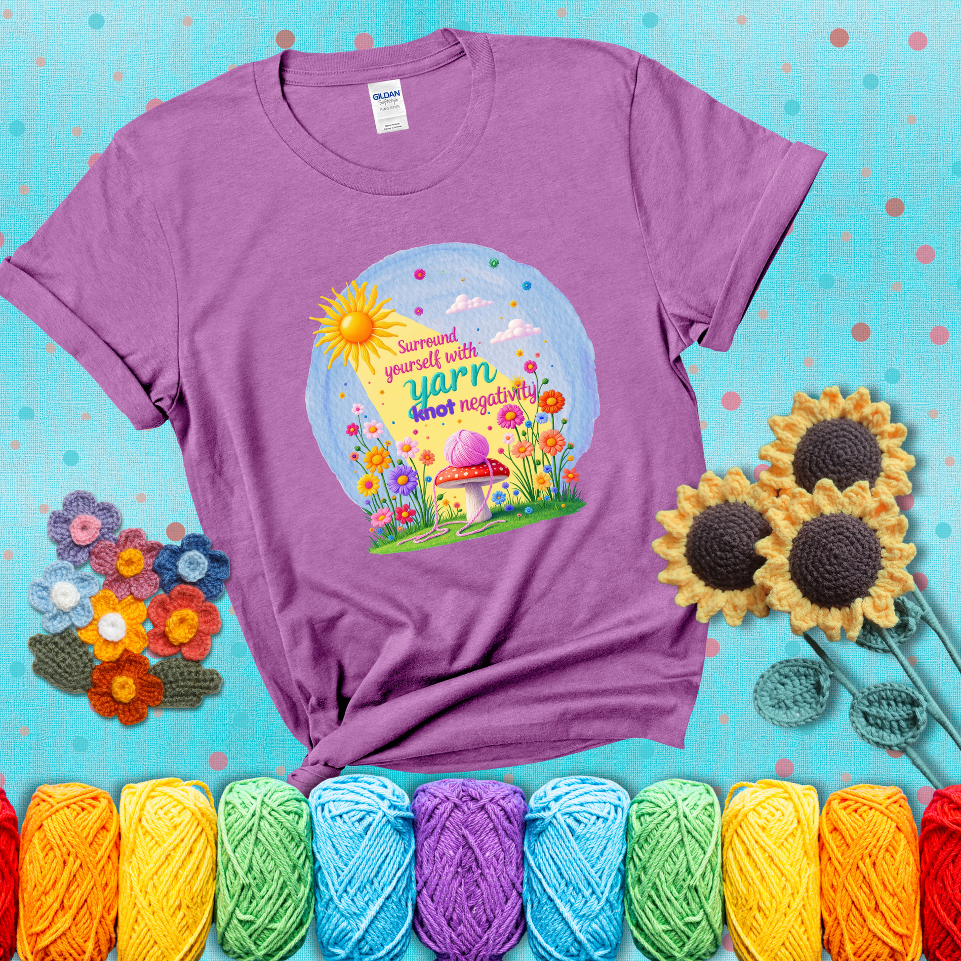 A happy spring garden scene with a sunbeam, flowers, and a pink yarn ball on a mushroom, with the quote "Surround yourself with yarn, knot negativity," showing a light purple tee with a teal sunflower background