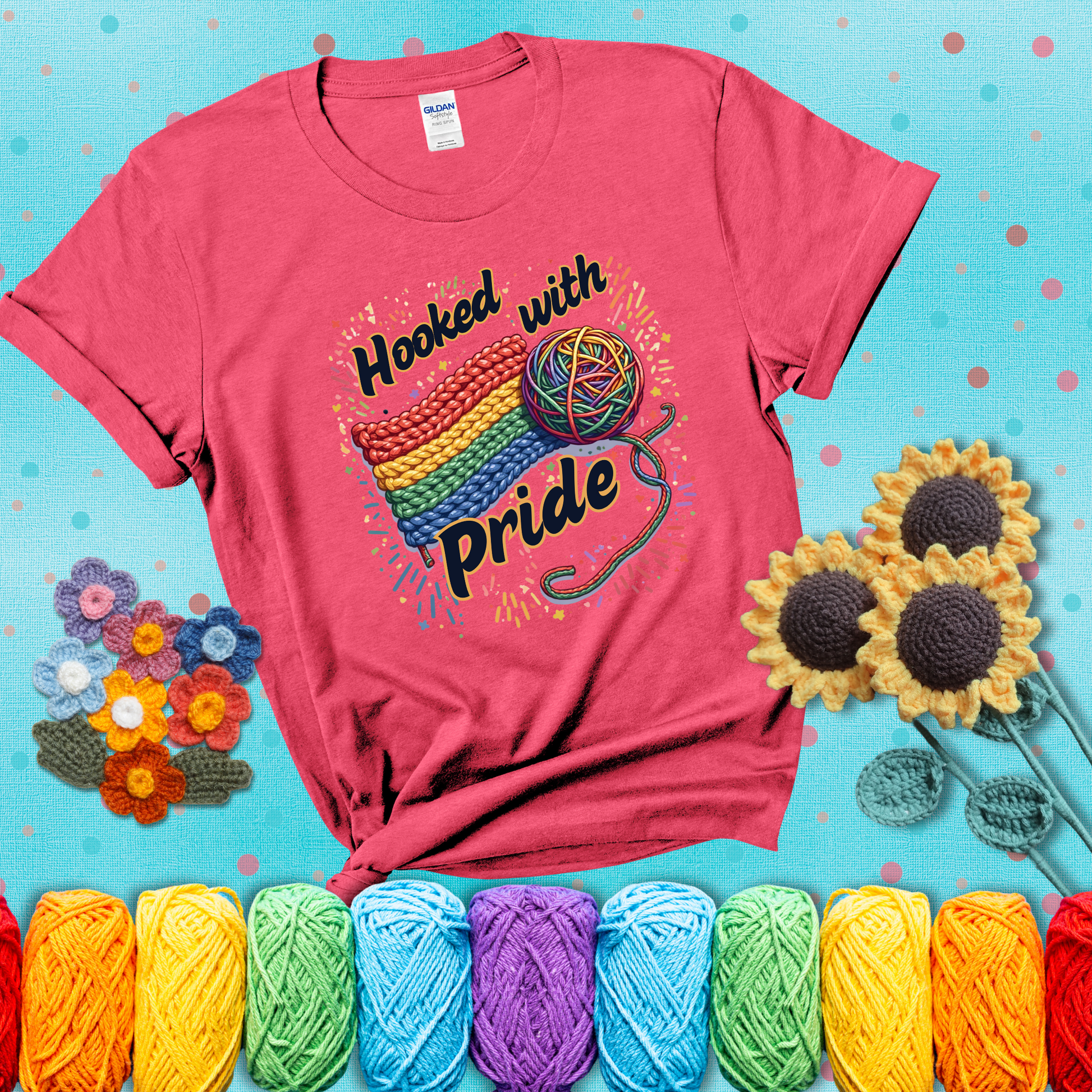 A rainbow-striped crochet swatch paired with a multicolor yarn ball and bold “Hooked With Pride” lettering. Confetti surrounds the vibrant scene showing a light red tee with a teal sunflower background