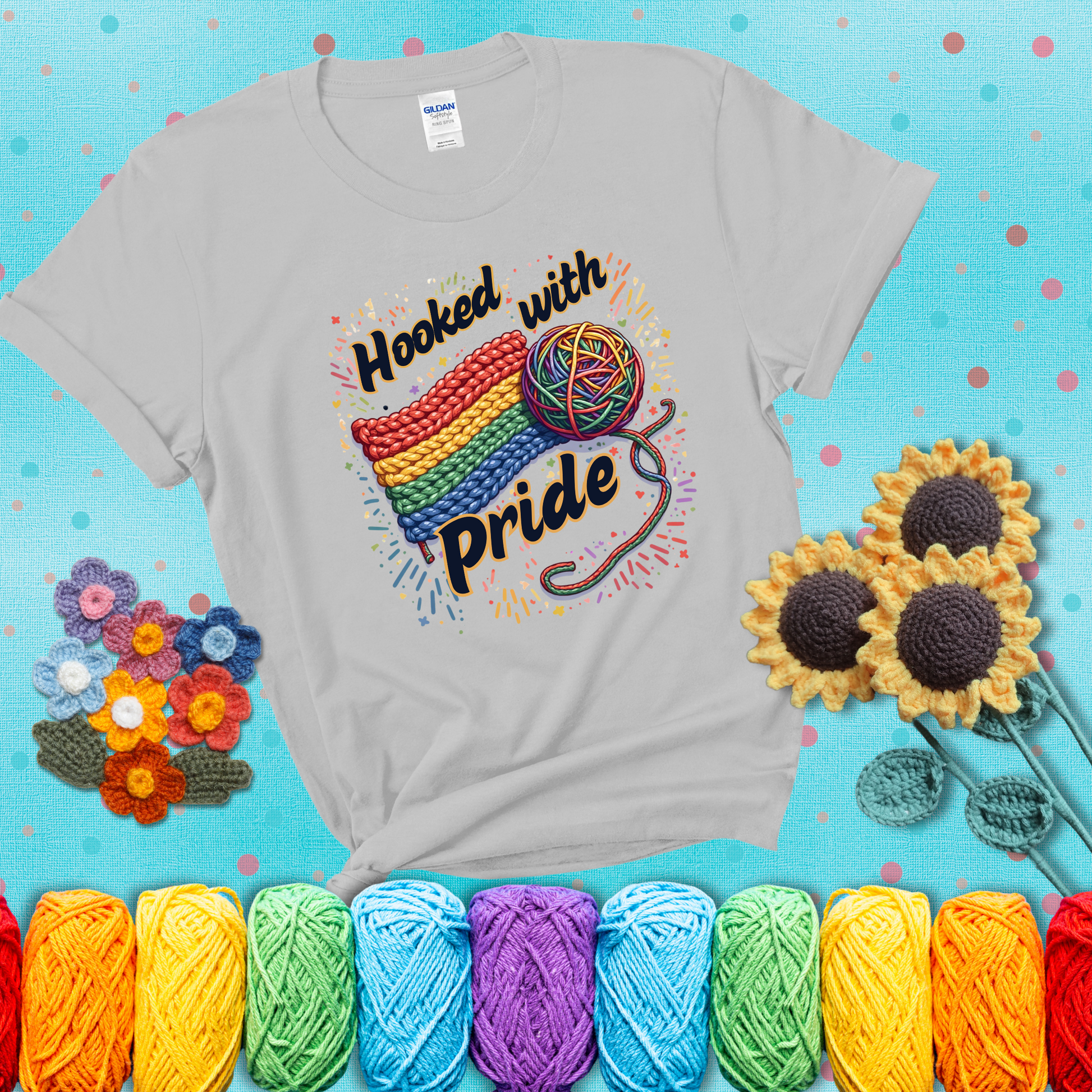 A rainbow-striped crochet swatch paired with a multicolor yarn ball and bold “Hooked With Pride” lettering. Confetti surrounds the vibrant scene showing a light grey tee with a teal sunflower background