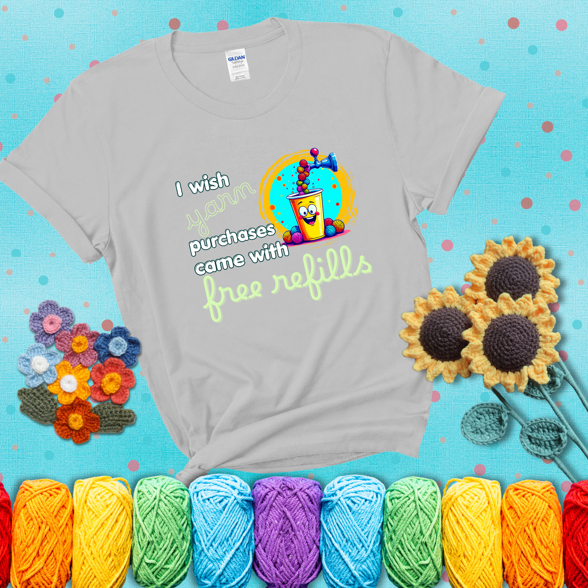 A bright yellow cup with a smiling face is being filled with colorful yarn balls from a soda machine, with the phrase “I wish yarn purchases came with free refills,” showing a light grey tee with a teal sunflower background