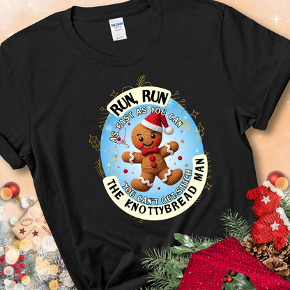 Black t-shirt with a crocheted gingerbread man in a Santa hat and the phrase “You Can’t Out-Stitch the Knottybread Man.”