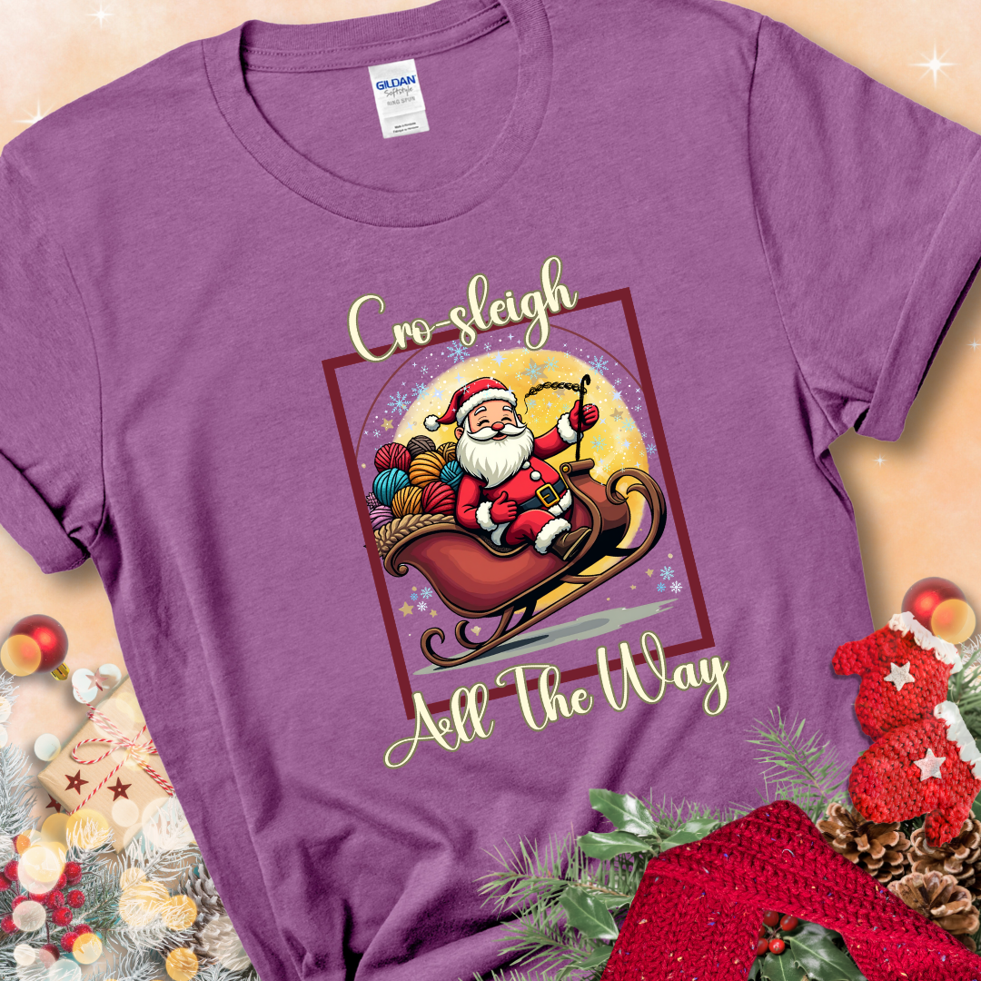 Heather Radiant Orchid t-shirt with Santa riding in a sleigh overflowing with colorful yarn and the phrase “Cro-Sleigh All The Way.”