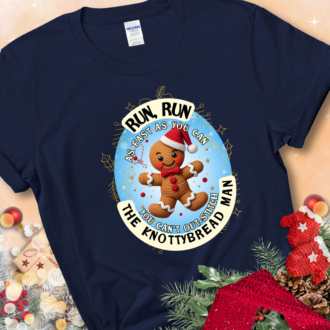 Navy Blue t-shirt with a crocheted gingerbread man in a Santa hat and the phrase “You Can’t Out-Stitch the Knottybread Man.”
