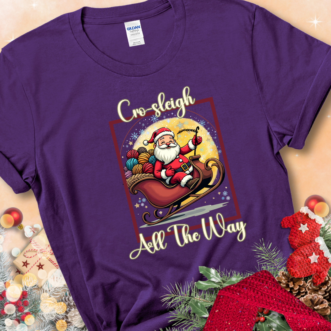 Purple t-shirt with Santa riding in a sleigh overflowing with colorful yarn and the phrase “Cro-Sleigh All The Way.”