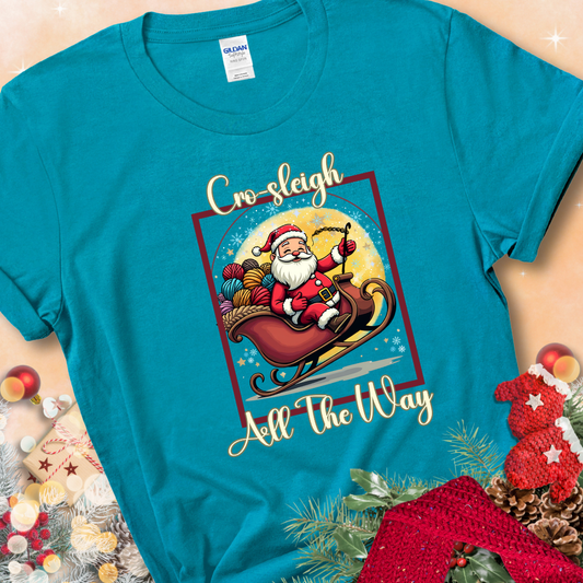 Tropical Blue t-shirt with Santa riding in a sleigh overflowing with colorful yarn and the phrase “Cro-Sleigh All The Way.”