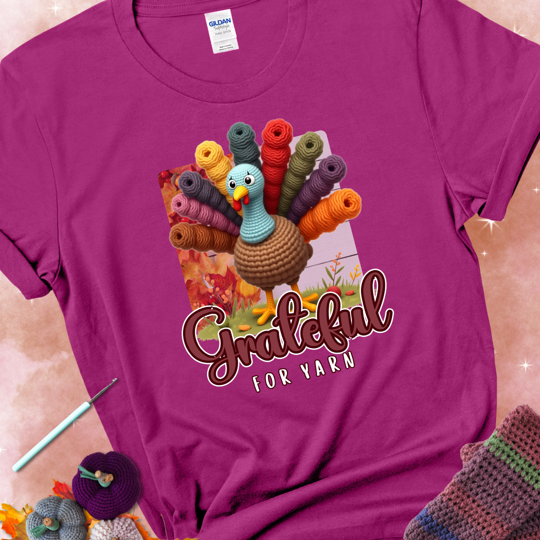 Antique heliconia t-shirt with a crocheted turkey, colorful yarn skeins for tail feathers, fall leaves, and the text “Grateful for Yarn.”