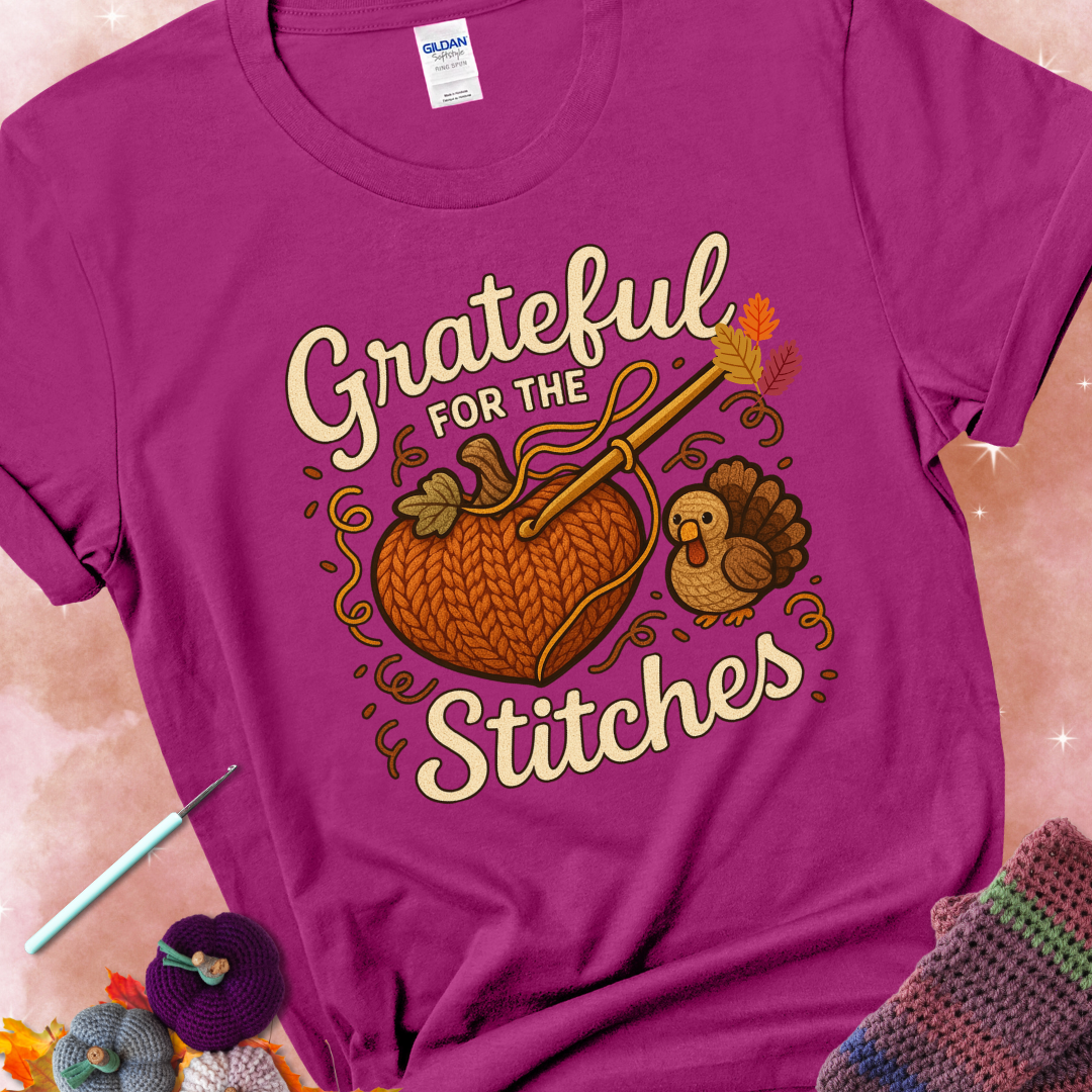 Antique Heliconia t-shirt with a crochet hook stitching a heart-shaped pumpkin, surrounded by yarn and a small turkey, with the phrase “Grateful for the Stitches.”