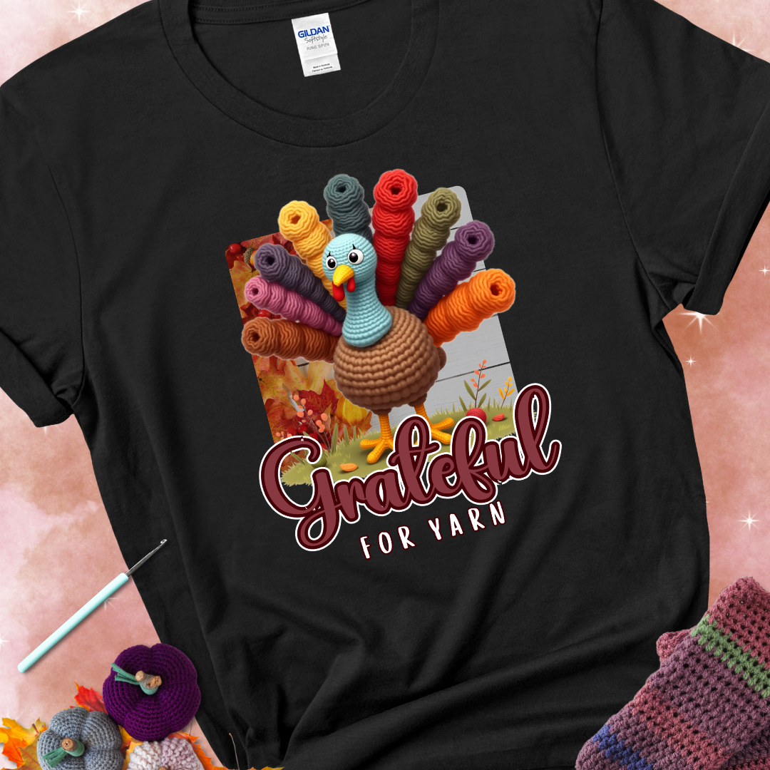 Black t-shirt with a crocheted turkey, colorful yarn skeins for tail feathers, fall leaves, and the text “Grateful for Yarn.”