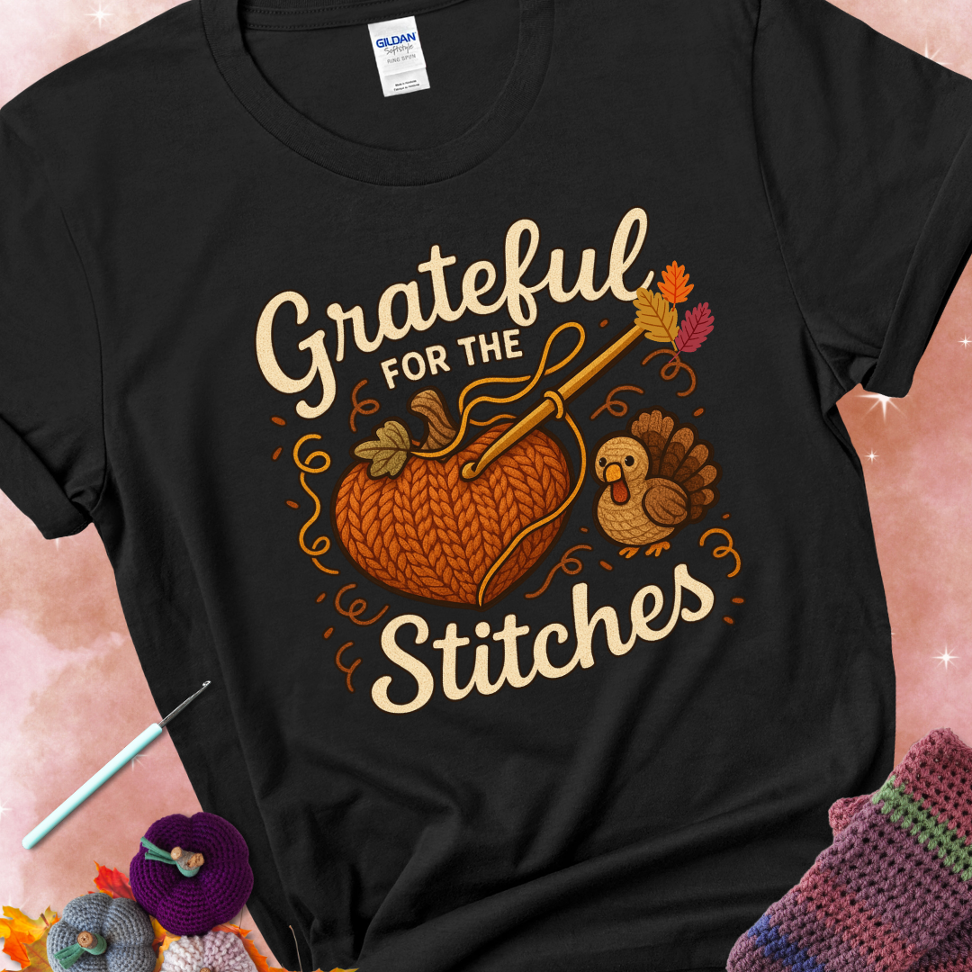Black t-shirt with a crochet hook stitching a heart-shaped pumpkin, surrounded by yarn and a small turkey, with the phrase “Grateful for the Stitches.”