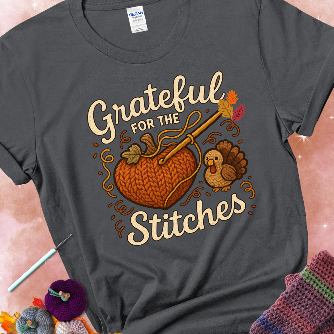 Charcoal t-shirt with a crochet hook stitching a heart-shaped pumpkin, surrounded by yarn and a small turkey, with the phrase “Grateful for the Stitches.”