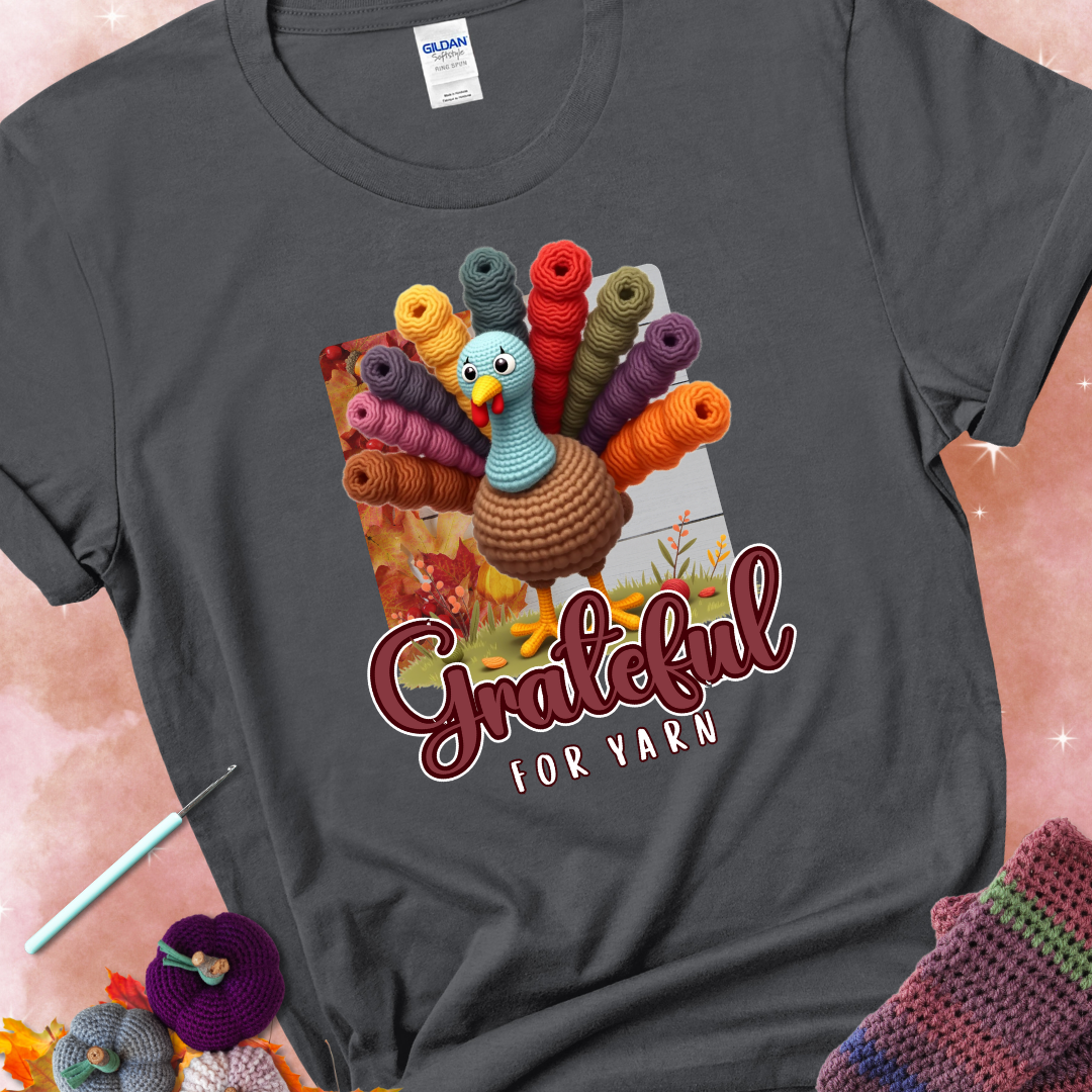 Charcoal t-shirt with a crocheted turkey, colorful yarn skeins for tail feathers, fall leaves, and the text “Grateful for Yarn.”