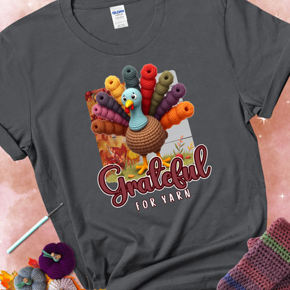 Charcoal t-shirt with a crocheted turkey, colorful yarn skeins for tail feathers, fall leaves, and the text “Grateful for Yarn.”
