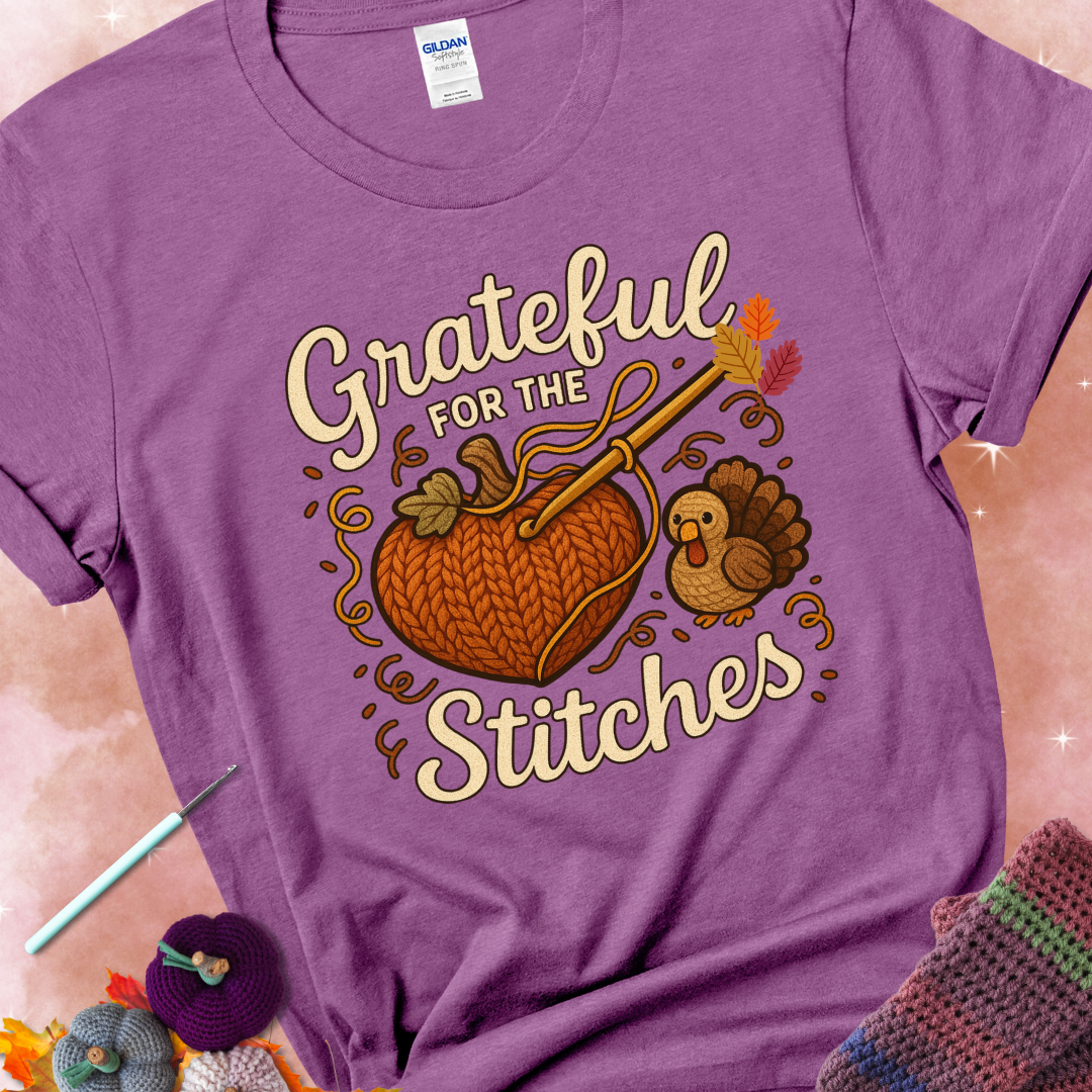 Heather Radiant Orchid t-shirt with a crochet hook stitching a heart-shaped pumpkin, surrounded by yarn and a small turkey, with the phrase “Grateful for the Stitches.”