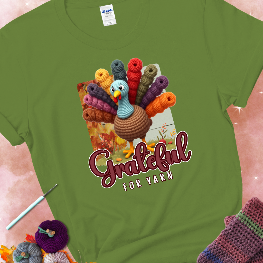 Kiwi t-shirt with a crocheted turkey, colorful yarn skeins for tail feathers, fall leaves, and the text “Grateful for Yarn.”