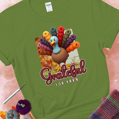 Kiwi t-shirt with a crocheted turkey, colorful yarn skeins for tail feathers, fall leaves, and the text “Grateful for Yarn.”