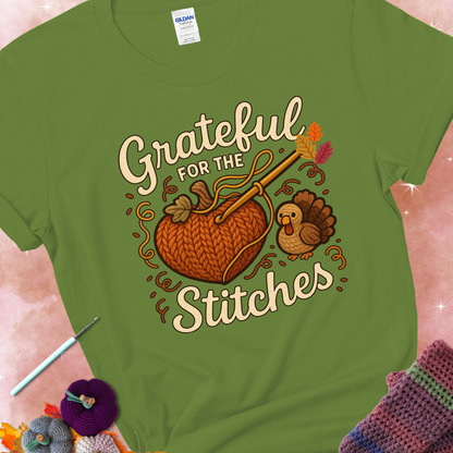 Kiwi t-shirt with a crochet hook stitching a heart-shaped pumpkin, surrounded by yarn and a small turkey, with the phrase “Grateful for the Stitches.”