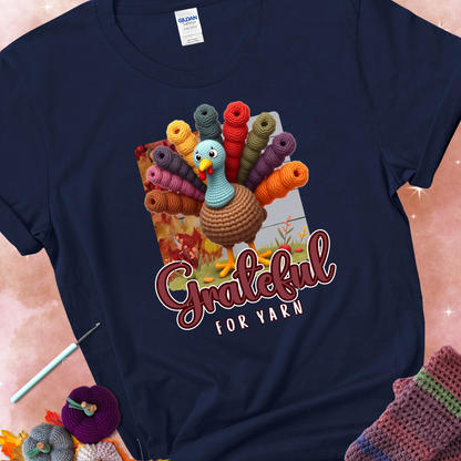 Navy t-shirt with a crocheted turkey, colorful yarn skeins for tail feathers, fall leaves, and the text “Grateful for Yarn.”