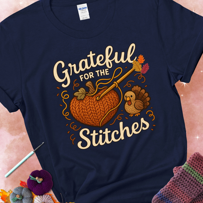 Navy t-shirt with a crochet hook stitching a heart-shaped pumpkin, surrounded by yarn and a small turkey, with the phrase “Grateful for the Stitches.”