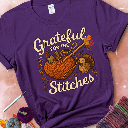 Purple t-shirt with a crochet hook stitching a heart-shaped pumpkin, surrounded by yarn and a small turkey, with the phrase “Grateful for the Stitches.”