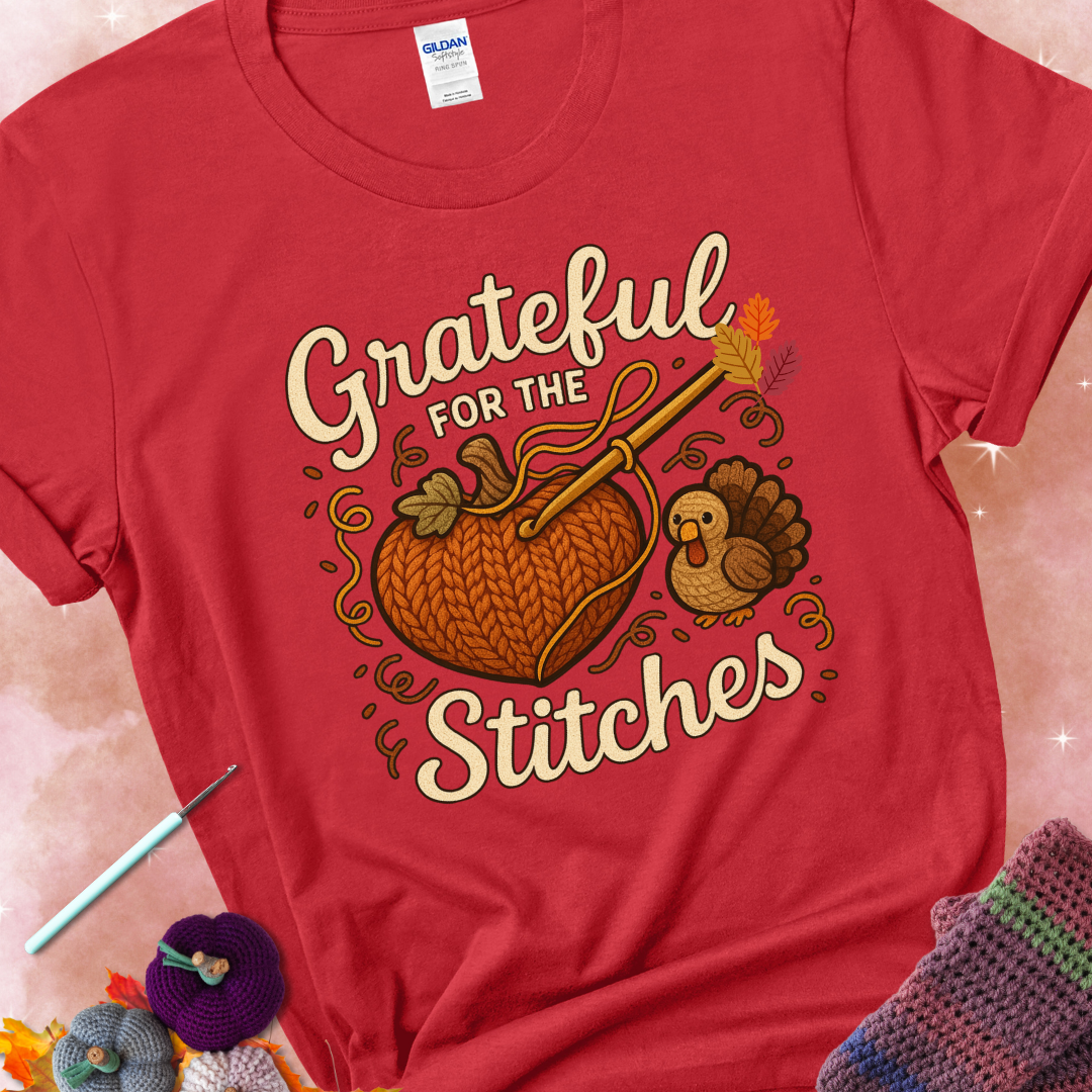Red t-shirt with a crochet hook stitching a heart-shaped pumpkin, surrounded by yarn and a small turkey, with the phrase “Grateful for the Stitches.”