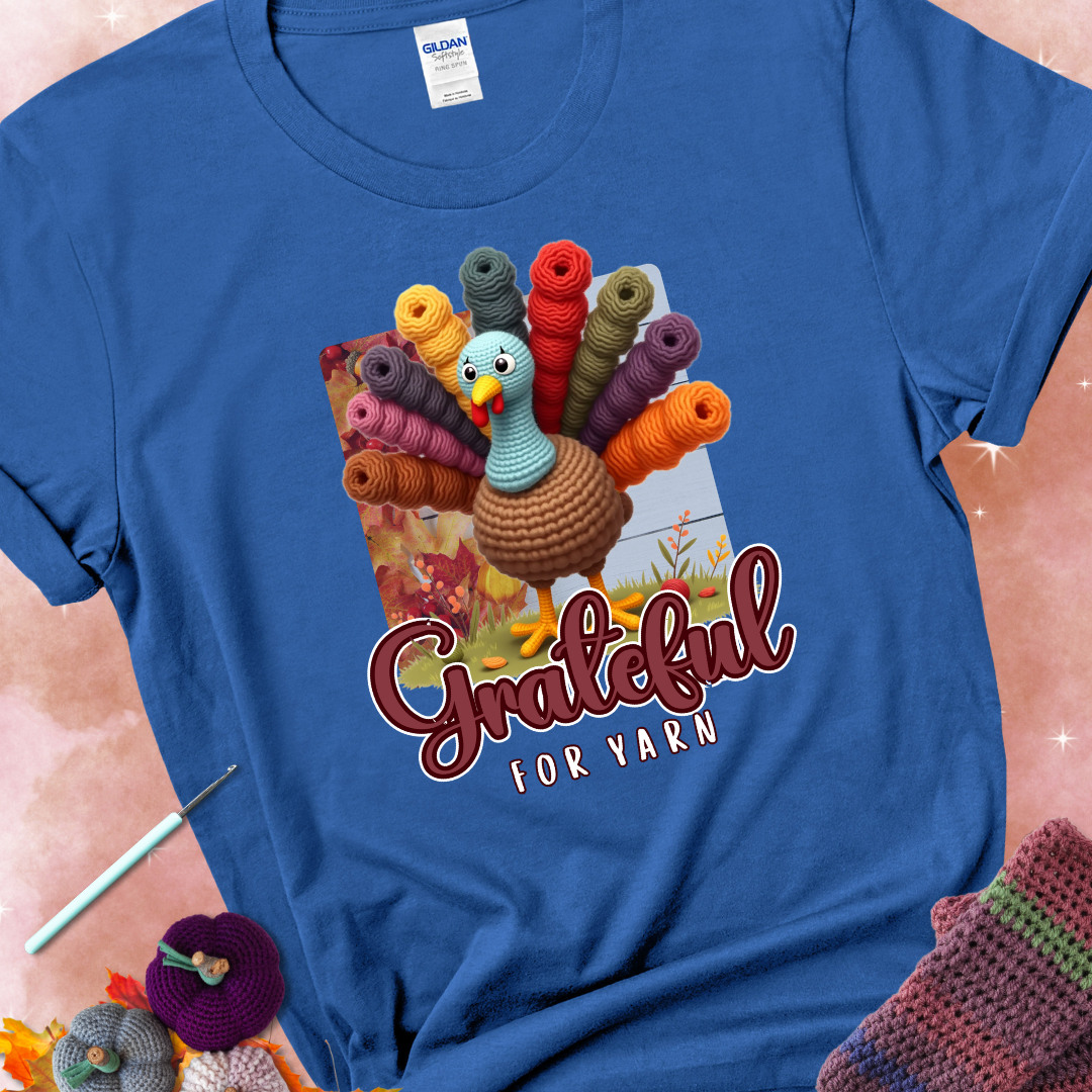 Royal blue t-shirt with a crocheted turkey, colorful yarn skeins for tail feathers, fall leaves, and the text “Grateful for Yarn.”