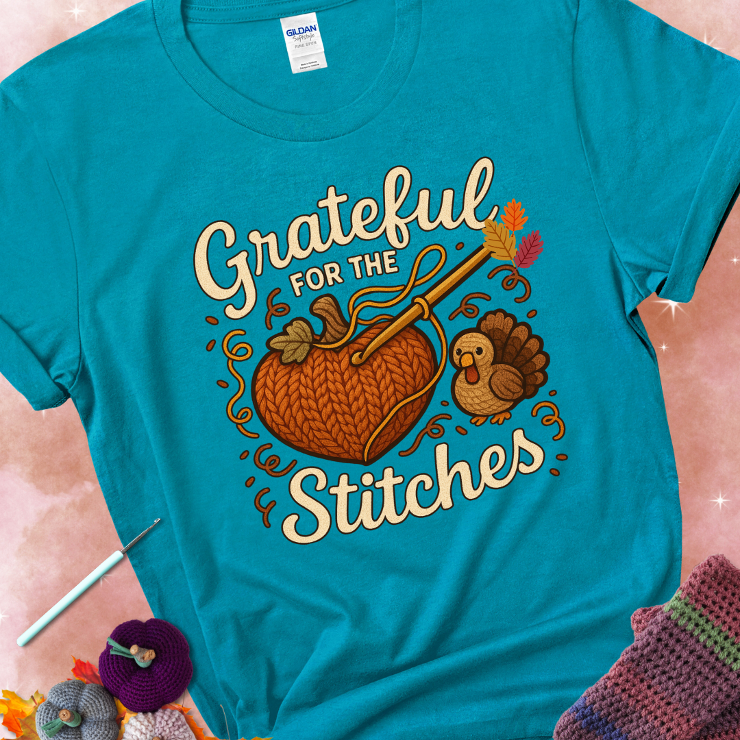 Tropical Blue t-shirt with a crochet hook stitching a heart-shaped pumpkin, surrounded by yarn and a small turkey, with the phrase “Grateful for the Stitches.”