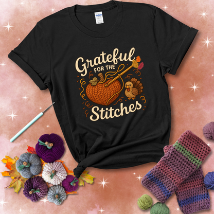 A cozy fall scene with a crochet hook stitching a heart-shaped pumpkin, surrounded by yarn and a small turkey, showing a black tee with a festive Fall background