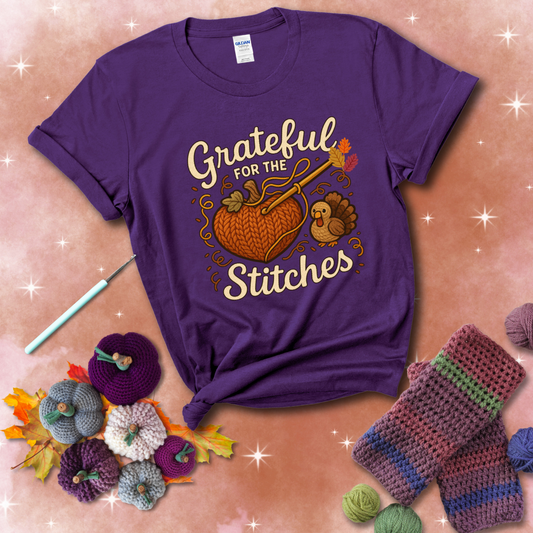 A cozy fall scene with a crochet hook stitching a heart-shaped pumpkin, surrounded by yarn and a small turkey, showing a purple tee with a festive Fall background