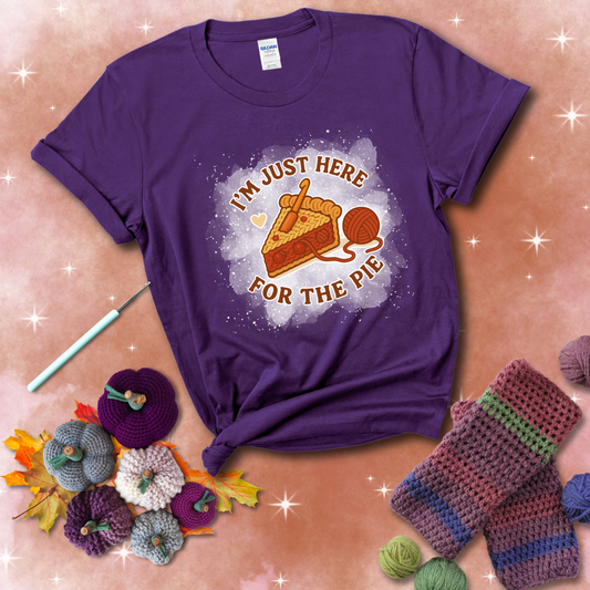 A slice of cherry pie with a crochet hook tucked in the filling and yarn trailing out, blending baking with crochet fun, showing a purple tee with a festive Fall background