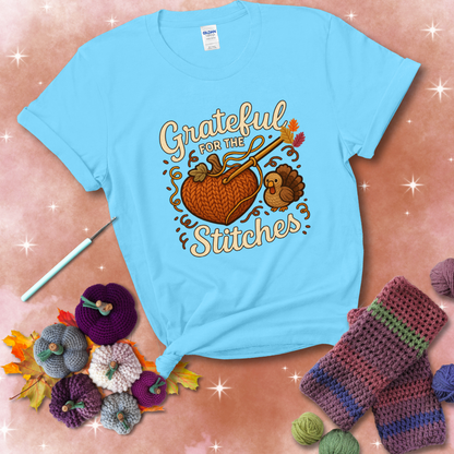A cozy fall scene with a crochet hook stitching a heart-shaped pumpkin, surrounded by yarn and a small turkey, showing a light blue tee with a festive Fall background