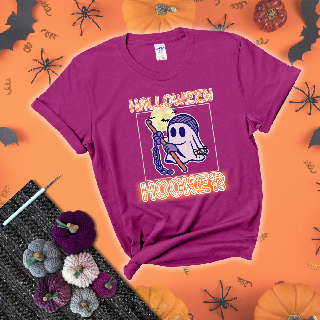 Cartoon ghost crocheter with a yarn ball head, crochet hook, bats, and text “Halloween Hooker,” a fun spooky tee for yarn lovers showing a magenta tee with a festive Halloween background