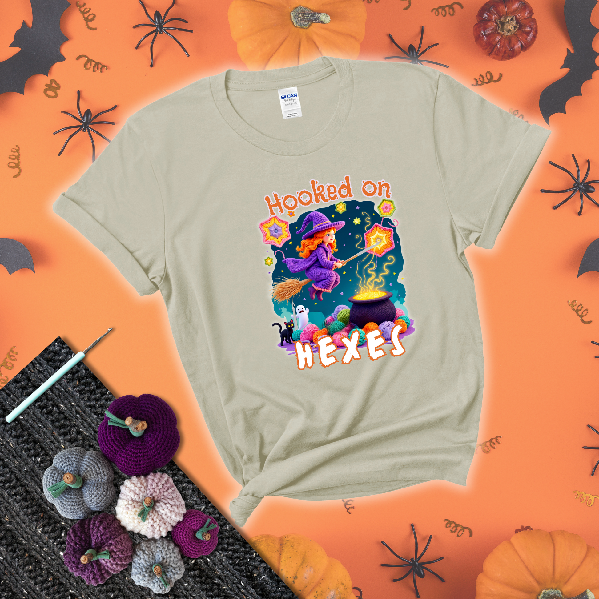 Witchy vibe with stars, hexagons, and a crochet hook. Text reads: “Hooked on Hexes.” A mystical and moody tee for fans of spooky stitches showing a beige tee with a festive Halloween background