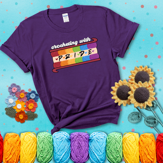 Yarn skeins in rainbow colors stacked in a hook shape. Text reads “Crocheting With Pride” showing a purple tee with a teal sunflower background
