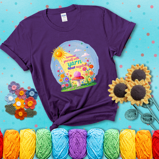 A happy spring garden scene with a sunbeam, flowers, and a pink yarn ball on a mushroom, with the quote "Surround yourself with yarn, knot negativity," showing a purple tee with a teal sunflower background