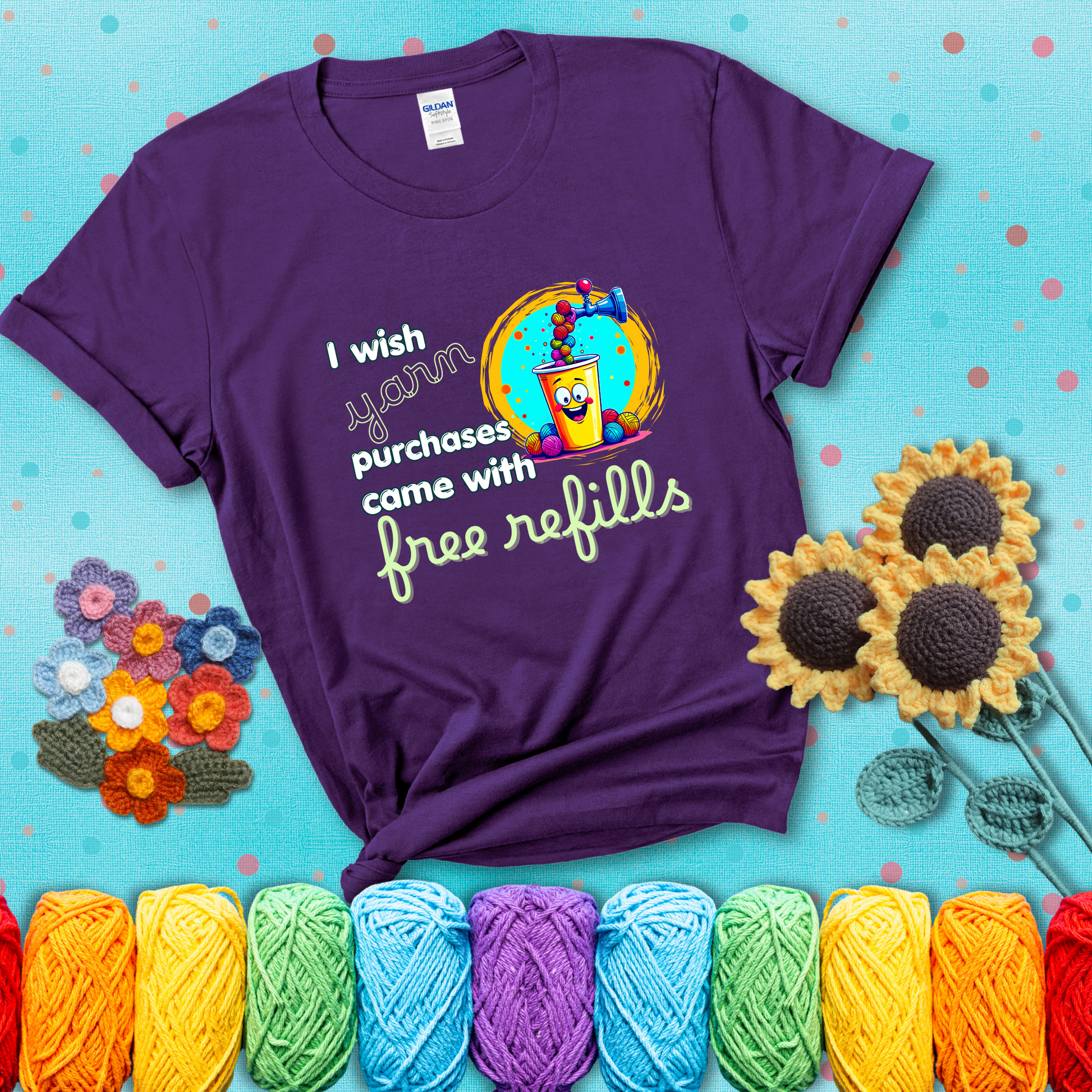 A bright yellow cup with a smiling face is being filled with colorful yarn balls from a soda machine, with the phrase “I wish yarn purchases came with free refills,” showing a purple tee with a teal sunflower background