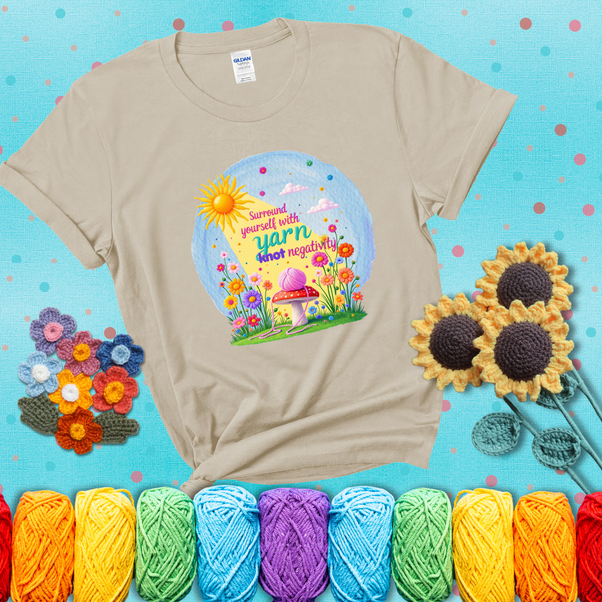 A happy spring garden scene with a sunbeam, flowers, and a pink yarn ball on a mushroom, with the quote "Surround yourself with yarn, knot negativity," showing a beige tee with a teal sunflower background