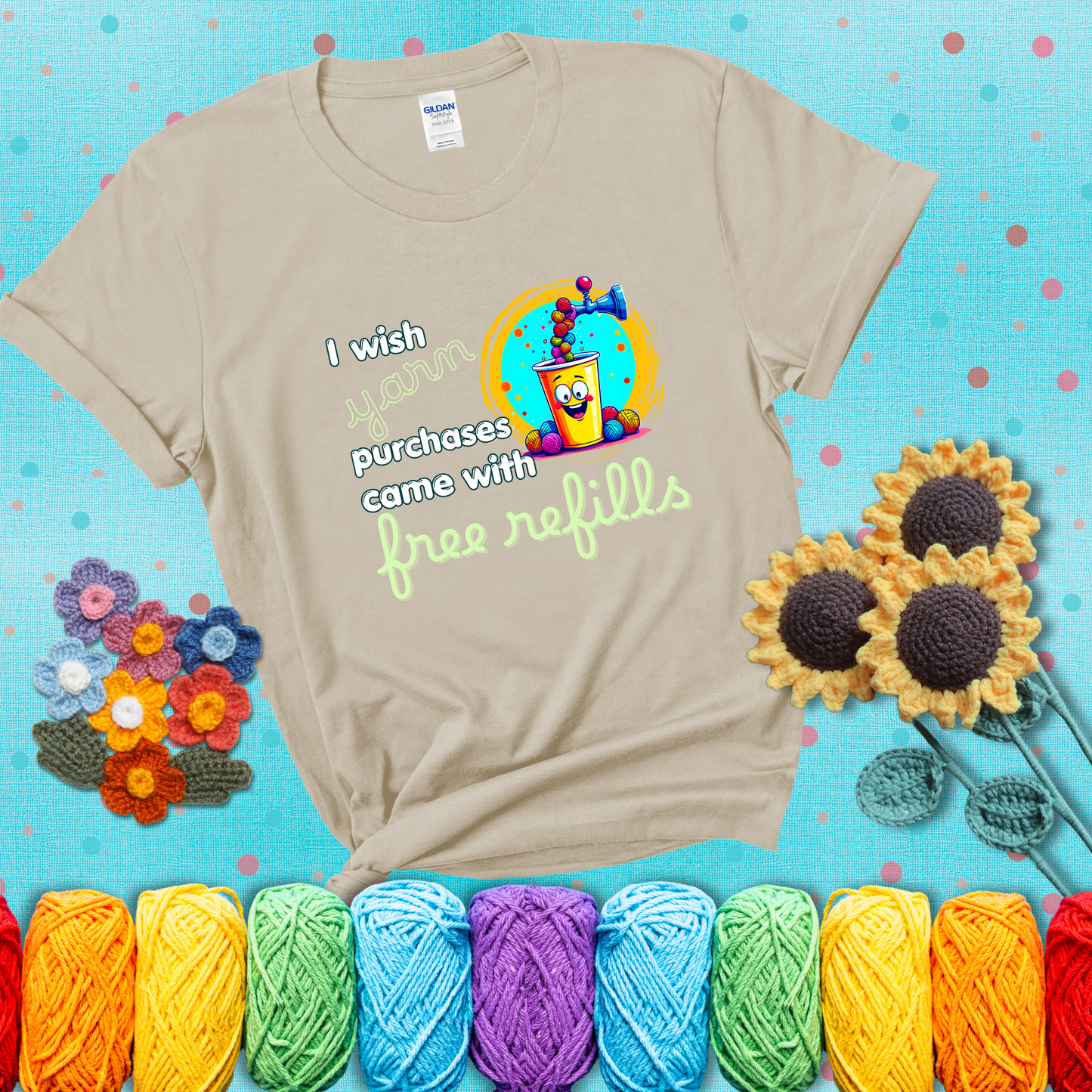 A bright yellow cup with a smiling face is being filled with colorful yarn balls from a soda machine, with the phrase “I wish yarn purchases came with free refills,” showing a beige tee with a teal sunflower background