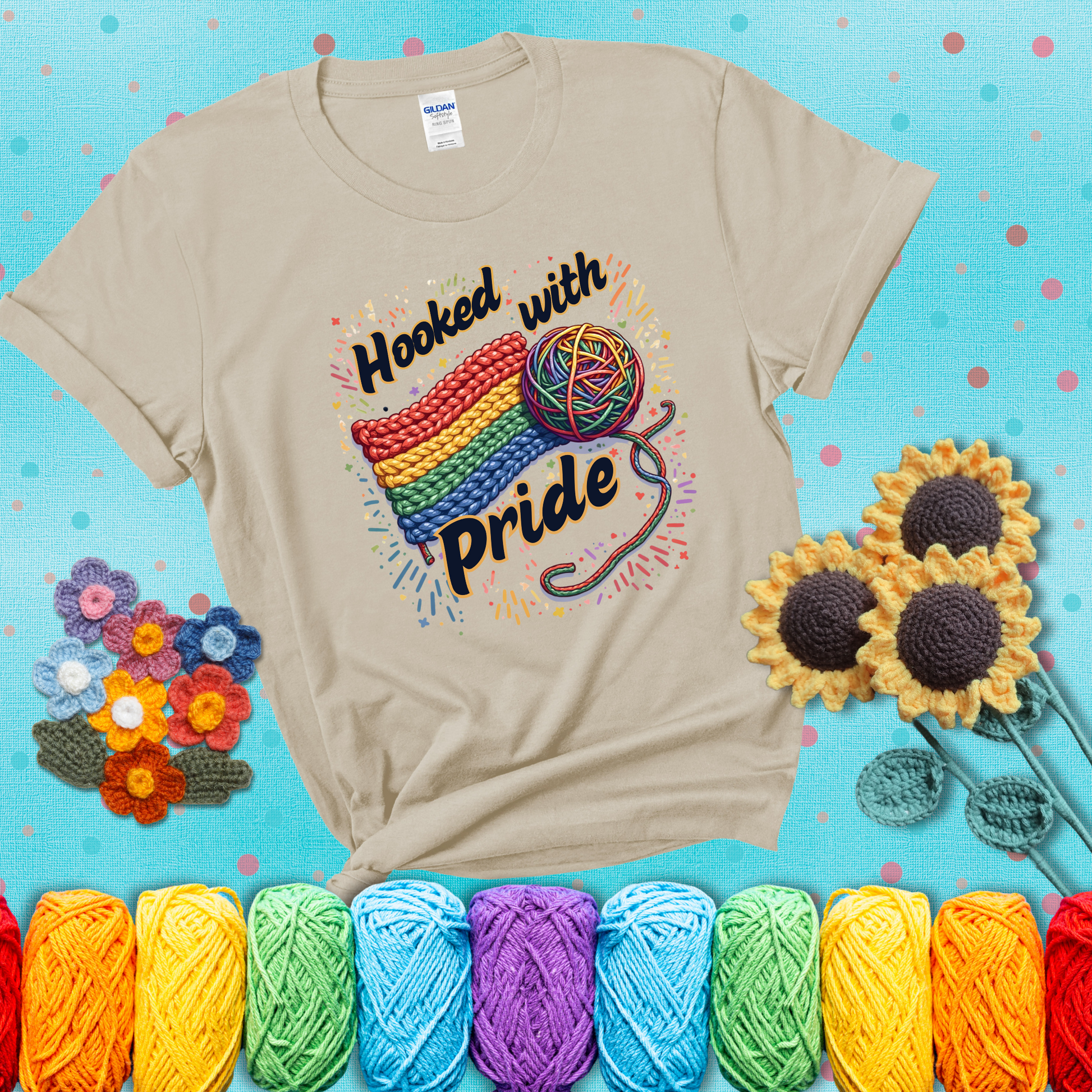 A rainbow-striped crochet swatch paired with a multicolor yarn ball and bold “Hooked With Pride” lettering. Confetti surrounds the vibrant scene showing a beige tee with a teal sunflower background
