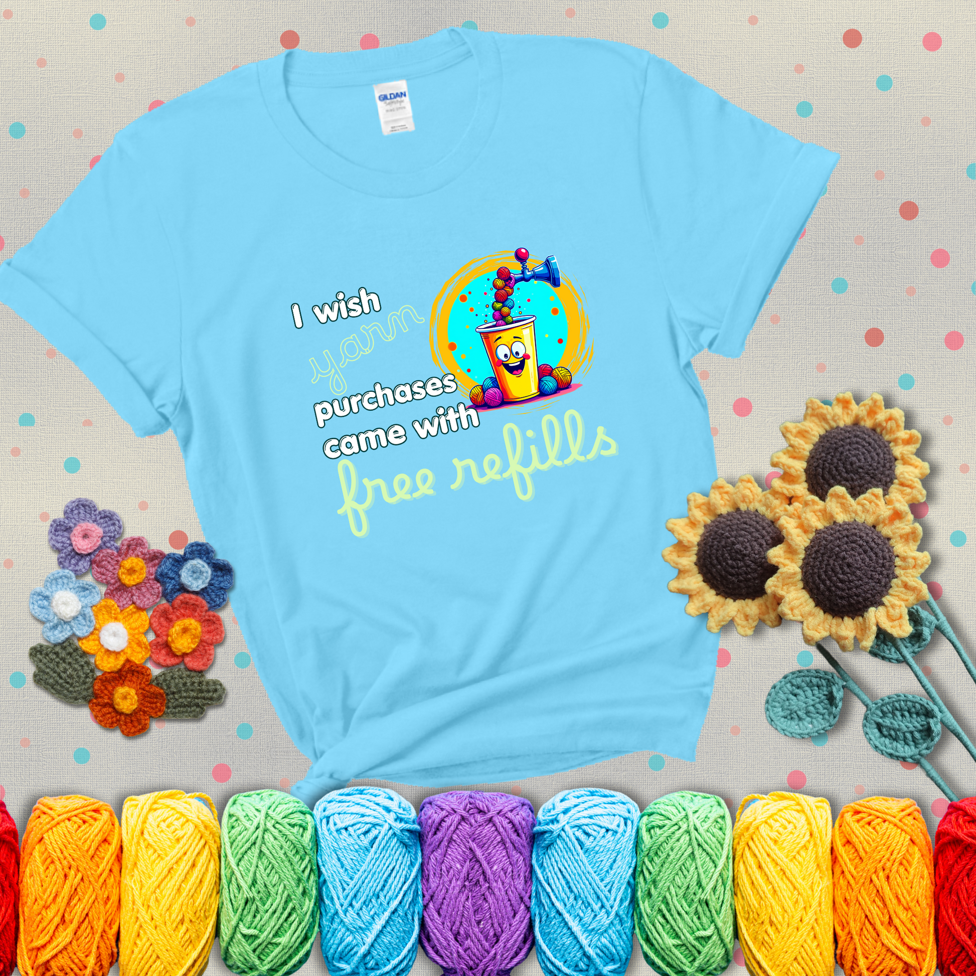 A bright yellow cup with a smiling face is being filled with colorful yarn balls from a soda machine, with the phrase “I wish yarn purchases came with free refills,” showing a light blue tee with grey sunflower background
