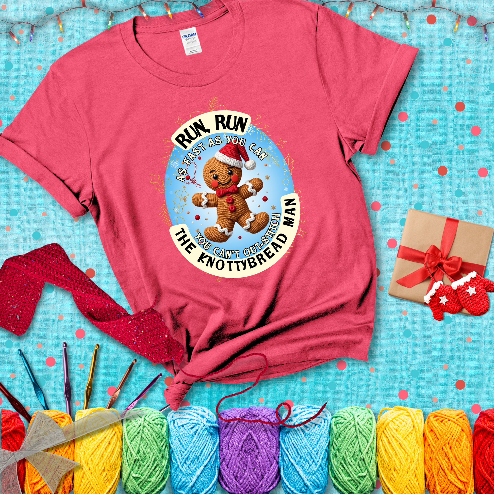 Cute crocheted gingerbread man in Santa hat with playful text: “Run, Run As Fast As You Can, You Can’t Out-Stitch the Knottybread Man.” A festive crochet pun shirt, showing a light red tee with a festive Christmas background